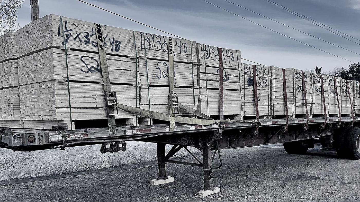 A flatbed trailer loaded with banded lumber, strapped down along its full length.