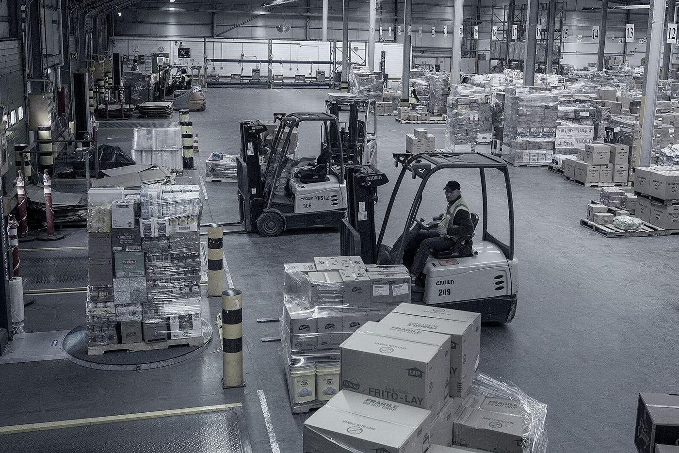 A forklift operator moving palletised freight across a busy warehouse floor.