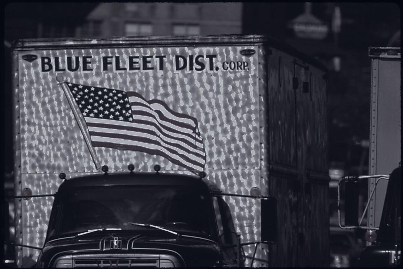 The front of a working truck with a flag mounted above the grille.